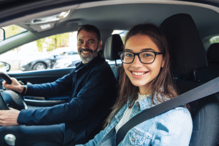 Fahrschülerin sitzt lächelnd mit Fahrlehrer während der Fahrstunde im Auto.