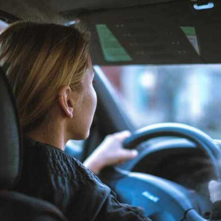 Person sitzt am Steuer eines Autos und hält beide Hände am Lenkrad.