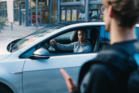 Fahrer im Auto hält Blickkontakt mit einem Fußgänger bei einer Verkehrssituation in der Stadt.